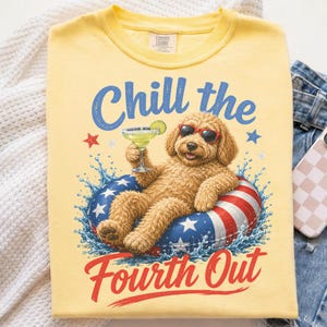 Op de afbeelding: Een lichtgeel t-shirt met een afbeelding van een golden doodle hond met een rode zonnebril, liggend in een rood-wit-blauwe zwemband met sterren terwijl deze een margarita vasthoudt. De tekst luidt Chill the Fourth Out in blauw en rood.