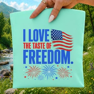 Peut inclure: Une pochette carrée en tissu vert menthe clair avec le texte bleu I LOVE THE TASTE OF FREEDOM, un graphique du drapeau américain et des illustrations de feux d'artifice rouges et bleus avec de petites étoiles sur la partie inférieure.