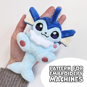 May include: A plush keyring of a blue creature with large dark eyes, a white neck ruff, and a fish-like tail. The plush features embroidered details and a metal ring. Text in the corner reads: PATTERN FOR EMBROIDERY MACHINES.