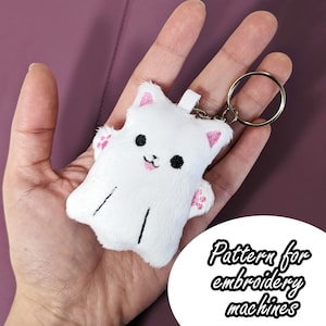 May include: White plush ghost keychain with pink ears and paw prints. The keychain is attached to a silver key ring. The image includes the text "Pattern for embroidery machines".