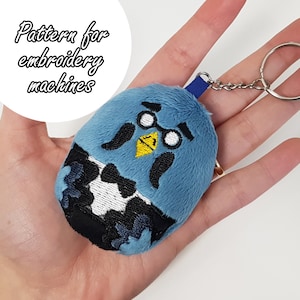May include: Blue plush keychain with embroidered details, including a mustache, glasses, bowtie, and a yellow beak. The keychain is attached to a silver key ring.
