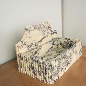 May include: A rectangular marble sink with a decorative back. The sink features a cream and brown marbled pattern. The front and sides have a vertical ribbed design. The sink is placed on a wooden surface.