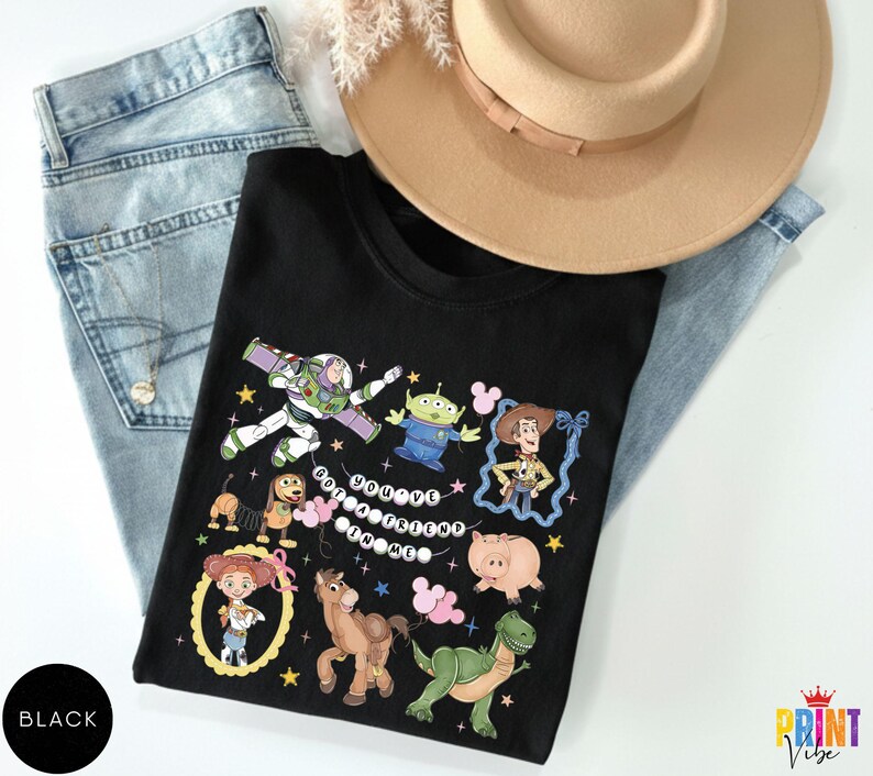 May include: A black t-shirt featuring a graphic print of various animated characters including a space ranger, a cowboy, a cowgirl, a green alien, a dinosaur, a pig, a horse, and a spring dog, with the text "YOU'VE GOT A FRIEND IN ME" in white.