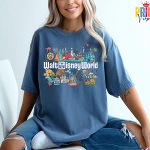 Puede incluir: Una camiseta azul con un gr&aacute;fico colorido de las atracciones de Walt Disney World. El dise&ntilde;o incluye el texto "Walt Disney World" en una fuente divertida, junto con ilustraciones de elementos ic&oacute;nicos del parque.