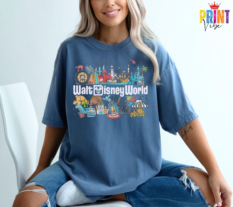 Puede incluir: Una camiseta azul con un gr&aacute;fico colorido de las atracciones de Walt Disney World. El dise&ntilde;o incluye el texto "Walt Disney World" en una fuente divertida, junto con ilustraciones de elementos ic&oacute;nicos del parque.