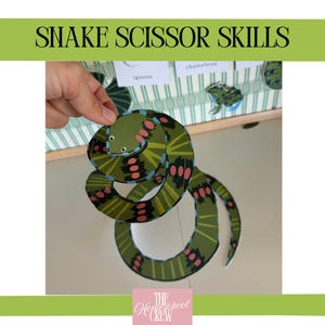 Könnte beinhalten: Eine grüne Papierschlange mit rosa und schwarzen Markierungen wird von einer Hand gehalten. Die Schlange ist Teil eines Bastelprojekts mit der Aufschrift "Snake Scissor Skills". Die Schlange befindet sich auf einer weißen Oberfläche.