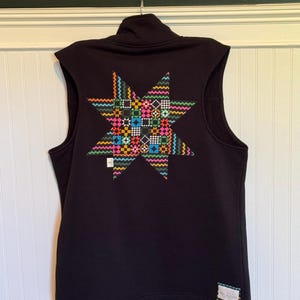 May include: A black sleeveless vest featuring a large, multi-colored star applique on the back. The star is composed of various geometric patterns in bright neon colors including pink, yellow, blue, and green. A small white label is visible on the lower right.