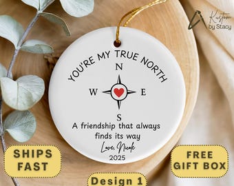 May include: White ceramic ornament with a compass design and the text "YOU'RE MY TRUE NORTH". The compass rose features a red heart. The ornament also includes the text "A friendship that always finds its way" and "Love, Nicole 2025".