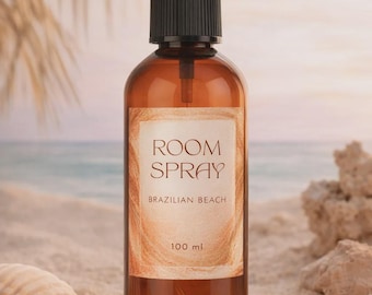 May include: A brown glass room spray bottle with a black cap and a white label that reads "ROOM SPRAY BRAZILIAN BEACH 100 ml." The bottle is set on a sandy surface with a seashell and rocks in the background.