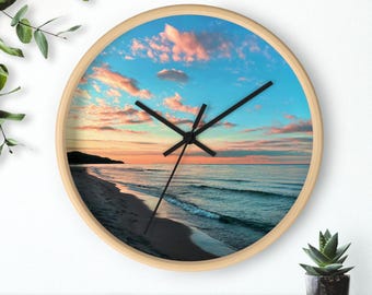 Reloj de pared con puesta de sol en la playa, de color rosa intenso y azul.
