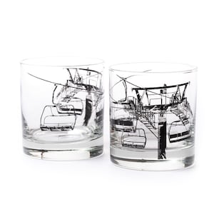 Two 11 ounce clear tumbler glasses with a heavy base. Black ink screen printing shows and image of a ski lift wrapping around the glass.