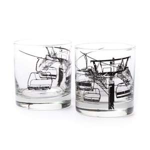 May include: Two clear glass tumblers with black and white illustrations of a ski lift. The ski lift is depicted with multiple chairs and a cable.
