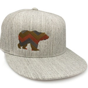 May include: A gray and white baseball cap with a brown, orange, and gray chevron bear design embroidered on the front.
