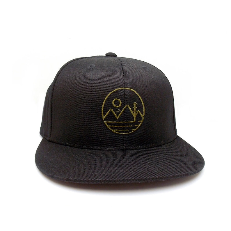 May include: Black baseball cap with a gold embroidered circle design featuring a mountain range, a sun, and a tree.