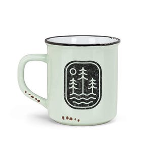 May include: A light green ceramic mug with a black and white design of three trees and a sun. The mug has a distressed look and a black rim.