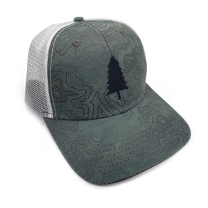 May include: A green trucker hat with a topographic map pattern and a black tree graphic. The hat features a white mesh back and a curved brim. The hat is a stylish accessory for outdoor enthusiasts.