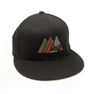 May include: Black fitted baseball cap with an embroidered design of three mountains in shades of brown, orange, and grey. The mountains have a stylised tree and a small cabin in the centre.