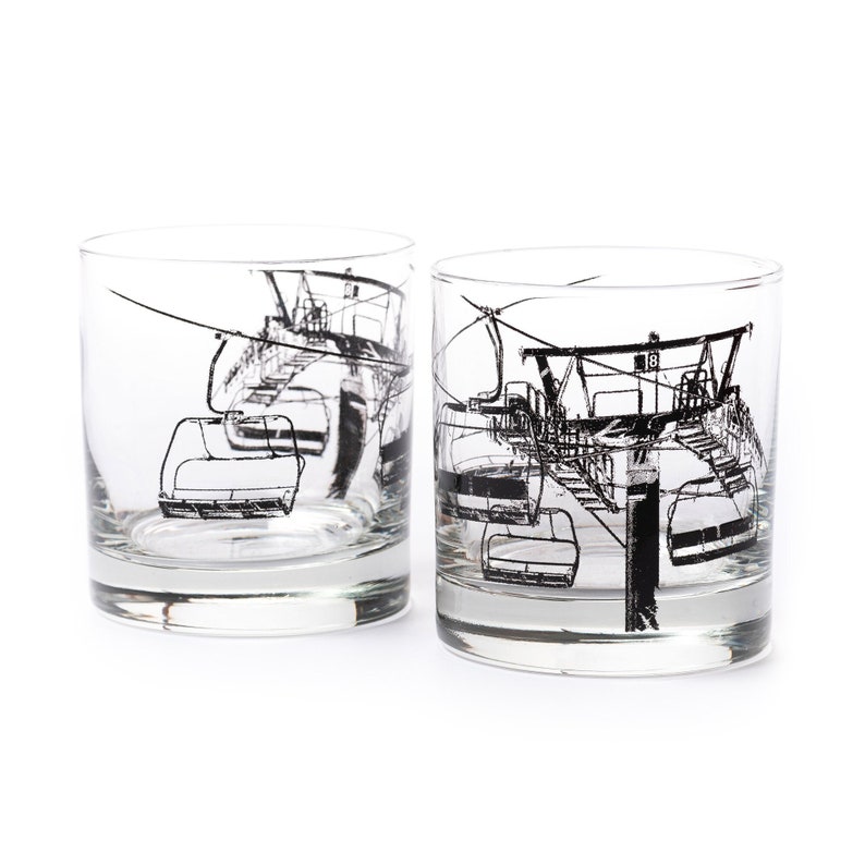 Two 11 ounce clear tumbler glasses with a heavy base. Black ink screen printing shows and image of a ski lift wrapping around the glass.
