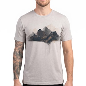 May include: A light gray heathered t-shirt featuring a central graphic of dark, layered mountain peaks with a textured, abstract design. The artwork includes fine vertical lines extending downward from the base of the mountains, creating a visual effect of depth and shadow across the chest area.