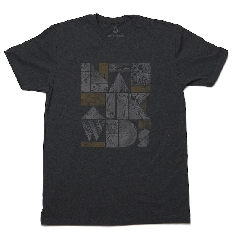 May include: A dark gray t-shirt with a geometric design featuring wood grain patterns in shades of gray and brown. The design is made up of various shapes, including squares, rectangles, and triangles.