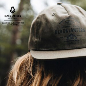 May include: A green baseball cap with a black logo that says "Black Lantern" and "Established 2013". The logo also features a mountain range and a campfire.