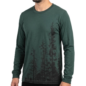 May include: A dark forest green long-sleeve t-shirt featuring a black graphic print of tall, slender pine trees extending from the bottom hem up the right side of the torso. The shirt has a classic crew neckline and fitted cuffs at the wrists.