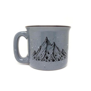 Puede incluir: Una taza de cerámica gris con un diseño de cordillera de montañas negras y motas blancas. La taza tiene un borde marrón.