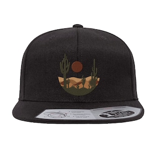 May include: Black fitted baseball cap with an embroidered desert landscape design featuring cacti, a sunset, and sand dunes.
