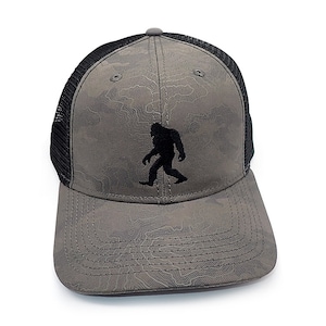 May include: A grey and black camouflage trucker hat with a black silhouette of Bigfoot on the front.