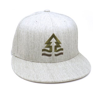 May include: A light gray flat-brimmed baseball cap with a structured crown. The cap features an embroidered design of a stylized tree in shades of olive green and brown on the front. The brim is curved and the cap is set against a white background.