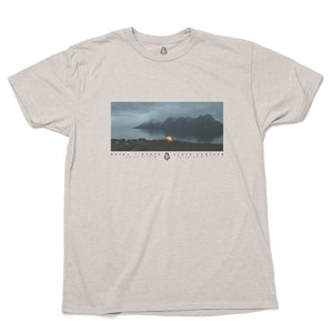 May include: A heather grey t-shirt with a graphic of a mountain range and a tent with a glowing orange light. The text "ROCKS - ROOTS - BLACK LANTERS" is printed below the image.