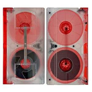 May include: Two clear plastic video tape cartridges with red and black reels. The cartridges have a transparent design, allowing the internal components to be visible. The edges of the cartridges are red. The reels are red and black.