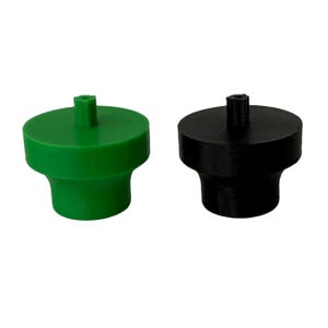 May include: Two bottle stoppers. One is bright green, the other is black. Both have a cylindrical base and a small, square peg on top. The stoppers are made of a solid material and are designed to fit into the opening of a bottle.