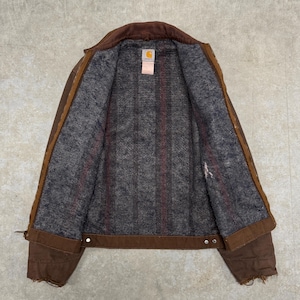 Puede incluir: Chaqueta de trabajo marr&oacute;n con cuello de pana y forro interior gris con estampado de cuadros. La chaqueta tiene cierre de botones y una peque&ntilde;a etiqueta con el logotipo. La chaqueta est&aacute; hecha de un material duradero y resistente.