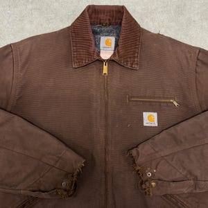 Puede incluir: Chaqueta de trabajo Carhartt marr&oacute;n con cuello de pana, bolsillo en el pecho con cremallera y dos parches cuadrados con el logotipo. La chaqueta tiene una cremallera de lat&oacute;n y pu&ntilde;os desgastados.