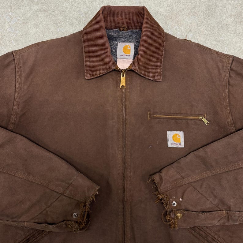 Puede incluir: Chaqueta de trabajo Carhartt marr&oacute;n con cuello de pana, bolsillo en el pecho con cremallera y dos parches cuadrados con el logotipo. La chaqueta tiene una cremallera de lat&oacute;n y pu&ntilde;os desgastados.