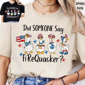 May include: A beige t-shirt featuring a graphic of four white ducks with patriotic accessories and the text Did SOMEONE Say FiReQuacker? The ducks hold an American flag, a hot dog, a drink, and wear star-spangled hats and sunglasses.