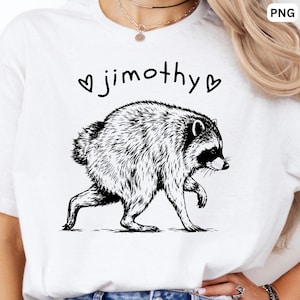 May include: A white t-shirt featuring a black line art illustration of a raccoon walking. Above the raccoon, the text "jimothy" is printed in a lowercase black font, flanked by two small black heart symbols on either side of the name.