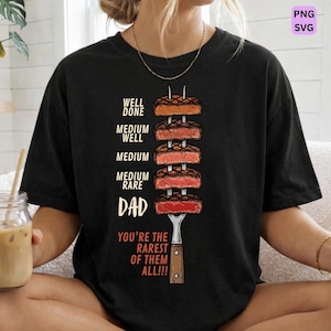 Könnte beinhalten: Schwarzes T-Shirt mit einer Grafik von Steak-Garstufen auf einer Gabel. Der Text lautet "WELL DONE, MEDIUM WELL, MEDIUM, MEDIUM RARE, DAD, YOU'RE THE RAREST OF THEM ALL!!!" in Weiß.