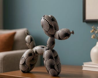 May include: A black and white balloon dog sculpture. The dog is made of a series of connected balloon shapes, with a fan-like pattern on each section. The sculpture is displayed on a wooden surface.