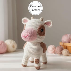 Könnte beinhalten: Eine gehäkelte Kuhfigur mit weißem Körper, braunen Flecken und rosa Akzenten an Nase und Ohren. Die Augen sind dunkelbraun. Der Text "Crochet Pattern" befindet sich in einem weißen Kreis über der Kuh.