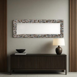 May include: A rectangular mirror with a decorative frame featuring a pattern of small, multicolored stones. The mirror hangs above a dark brown wooden cabinet with vertical grooves. A lamp with a brown base and a cream-colored shade sits on the cabinet.