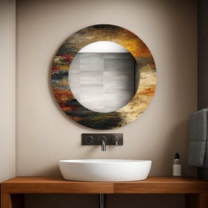 May include: A round mirror with a colorful abstract design in shades of brown, orange, and yellow. The mirror is mounted above a white, oval-shaped sink. The sink sits on a wooden countertop with a black faucet.