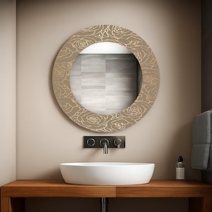 Peut inclure: Miroir rond décoratif avec un motif floral dans une salle de bain. Le miroir a un cadre beige avec des motifs de roses dorées. En dessous, un lavabo ovale blanc sur un comptoir en bois. Un robinet et une fixation murale noirs sont visibles.
