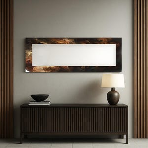 Puede incluir: Un espejo de pared rectangular con un centro blanco y un borde marrón y dorado en forma de nube. Debajo, un mueble marrón oscuro con líneas verticales, un cuenco negro y una lámpara con una pantalla beige.