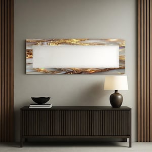 May include: A rectangular wall art piece with a white center and a gold and white marble-like border. Below, a dark brown wooden cabinet with vertical grooves, a black bowl, and a lamp with a beige shade.