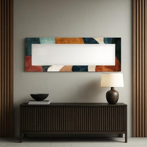 Può includere: Uno specchio da parete rettangolare con un design astratto nei toni del verde acqua, ruggine e blu navy. Lo specchio è montato sopra un mobile marrone scuro a coste. Una lampada con base marrone e paralume color crema è sul mobile.