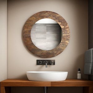 May include: A circular mirror with a textured, brown frame is mounted above a white, oval sink. The sink rests on a wooden vanity unit, with a black tap and control panel. The bathroom has a neutral colour scheme.