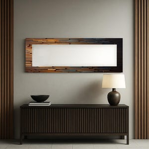 Puede incluir: Un espejo rectangular con un marco de mosaico de madera en tonos marrón, dorado y negro cuelga sobre un mueble marrón oscuro. Una lámpara con una pantalla de color crema está sobre el mueble. Un cuenco negro y libros también están en el mueble.