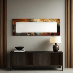 Könnte beinhalten: Ein rechteckiges abstraktes Gemälde mit weißer Mitte und farbenfrohem, strukturiertem Rand in Braun-, Orange- und Rottönen. Darunter ein dunkelbrauner Holzschrank mit vertikalen Rillen und eine Lampe mit cremefarbenem Schirm.